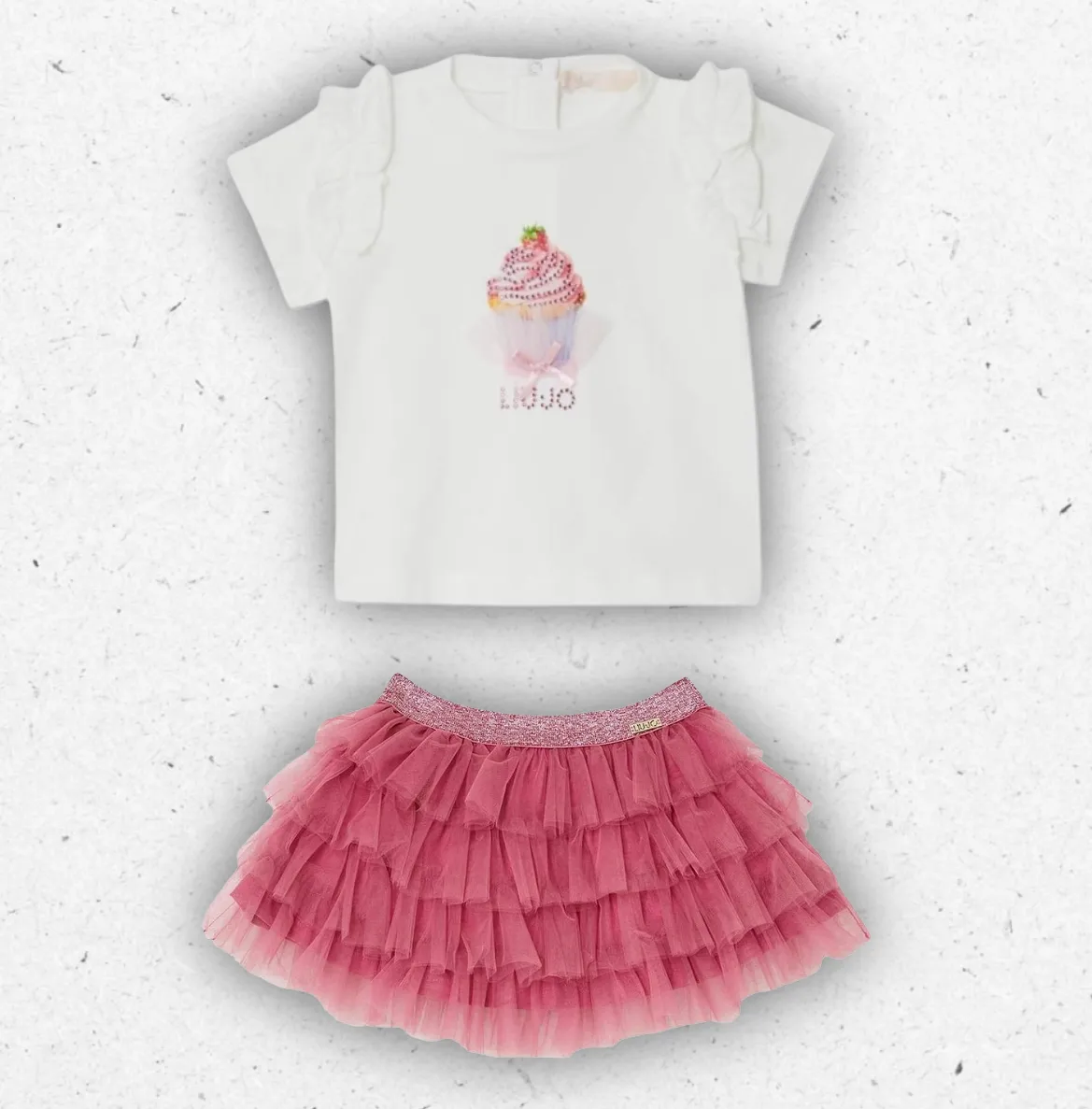 Completo elegante da bambina due pezzi firmato Liu Jo, visibile nel file composto da una t-shirt a maniche corte color panna con voulant sulle spalle e stampa di un cupcake in strass rosa, abbinata