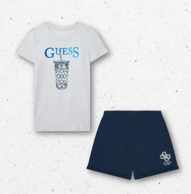 Completo da ragazza firmato Guess composto da una t-shirt a maniche corte celeste con maxi stampa frontale luminosa e scritte blu metalliche, abbinata a un pantaloncino short sportivo di colore blu navy con logo monogramma ricamato sul fondo della gamba s