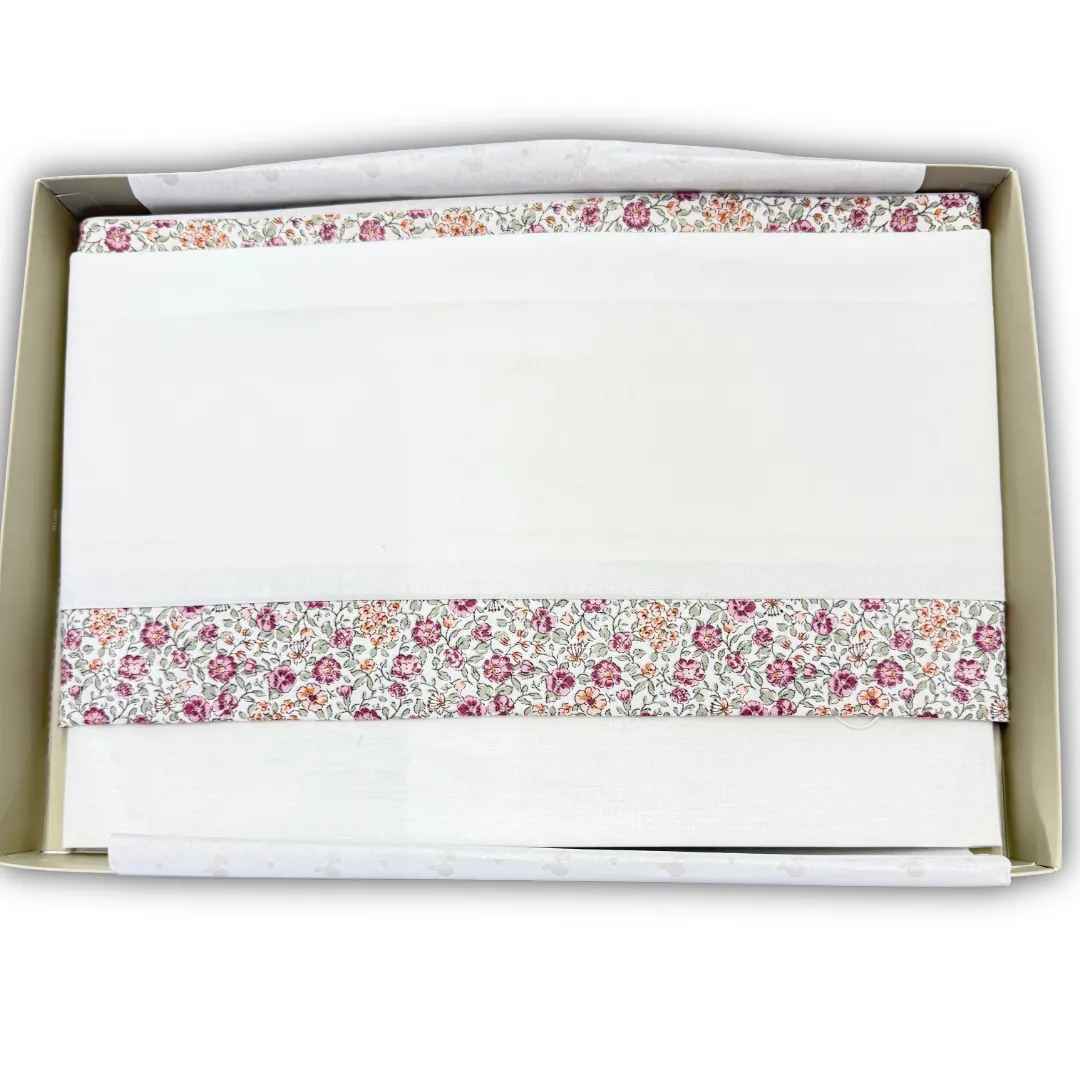 Set di biancheria o copertina Lalalù per neonata, di colore bianco panna, ripiegata in scatola con fascia decorativa floreale (rosa e verde).