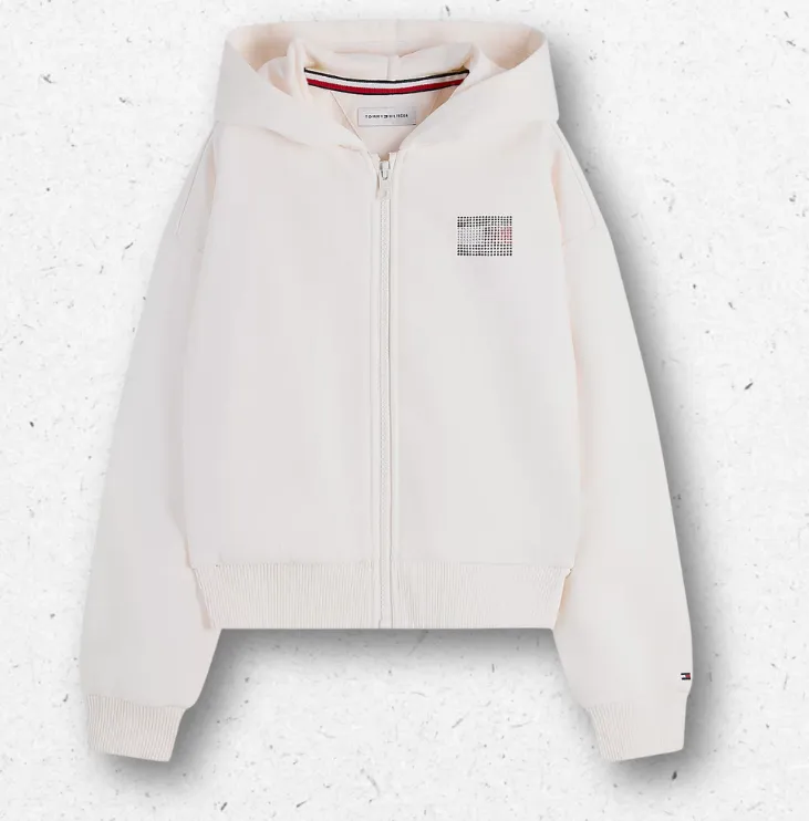 Felpa bianca da ragazza con cappuccio e zip firmata Tommy Hilfiger, caratterizzata da patch logo sul petto e maxi scritta posteriore "TOMMY" realizzate in strass colorati.