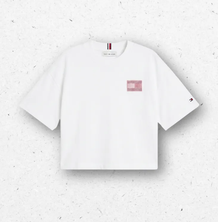 T-shirt bianca a maniche corte da ragazza firmata Tommy Hilfiger, con patch logo rettangolare sul petto impreziosita da brillantini rosa