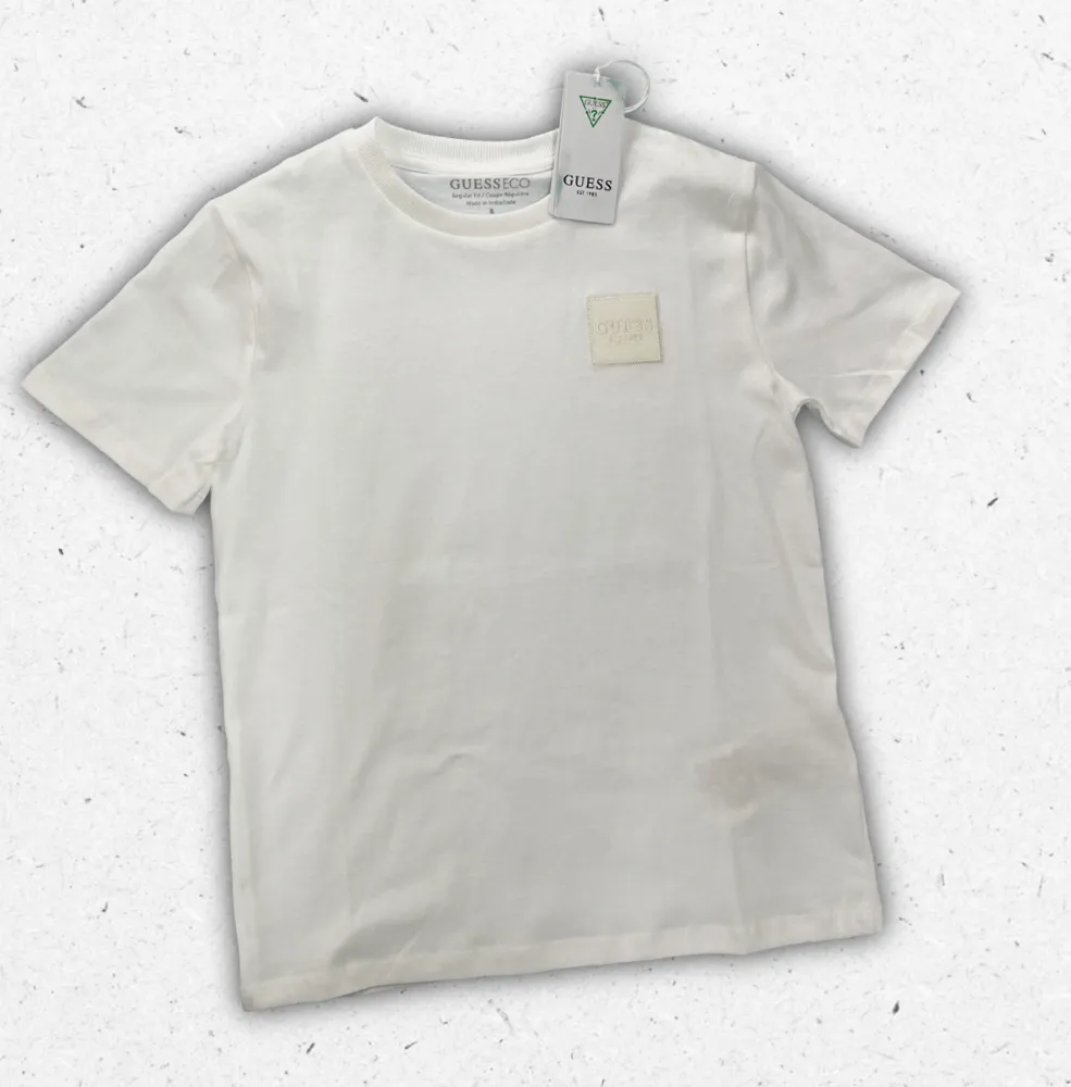 T-shirt bianca Guess da ragazzo in puro cotone con logo a triangolo iconico stampato centralmente sul petto.