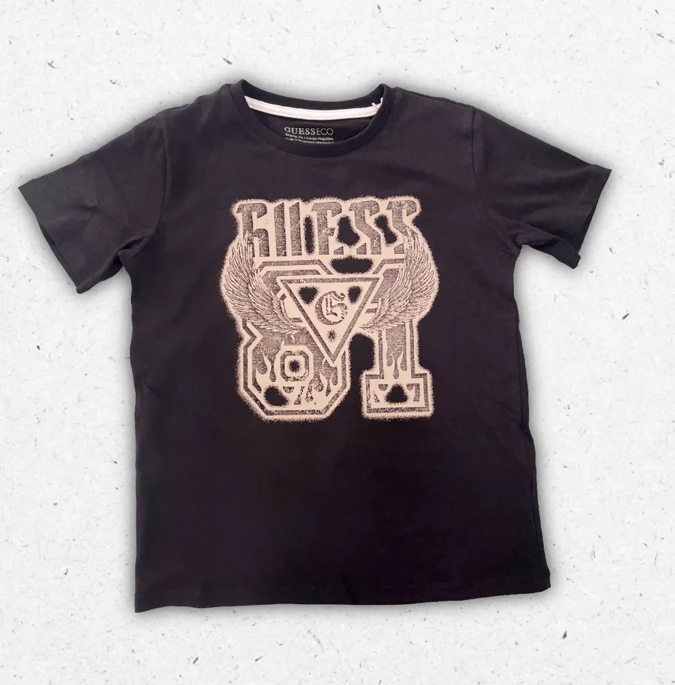 T-shirt Guess da ragazzo in cotone mostrata nelle colorazioni nera e bianca con stampa logo centrale sul petto.