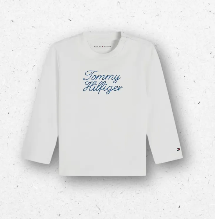 T-shirt a maniche lunghe bianca da neonato firmata Tommy Hilfiger, con scritta logo blu ricamata in corsivo sul petto e bottoni sulla spalla.