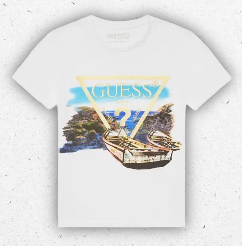 T-shirt da ragazzo a maniche corte di colore bianco firmata Guess, modello a girocollo con stampa frontale di un paesaggio di mare sovrastato dall'iconico logo a triangolo con profili color oro lucido.