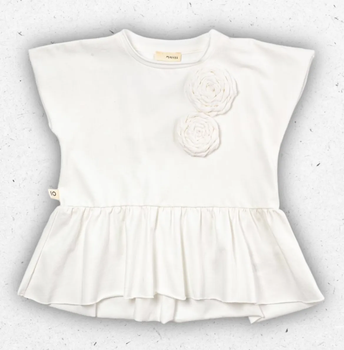 T-shirt smanicata da bambina Maperò color panna in cotone con due fiori applicati sul petto, volant sul fondo e logo laterale.